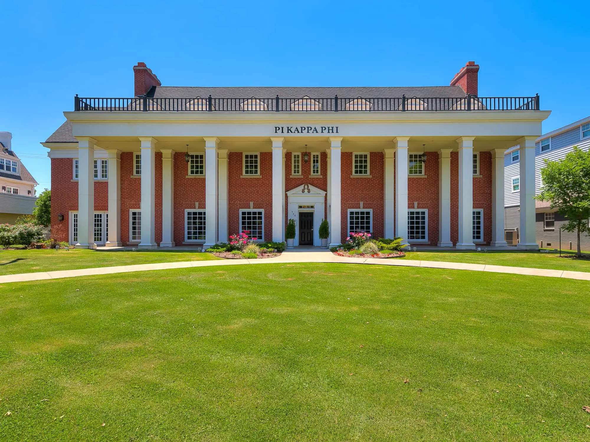The chapter house from the front lawn: a red brick building of two floors with a white columned portico and PI KAPPA PHI lettered across it