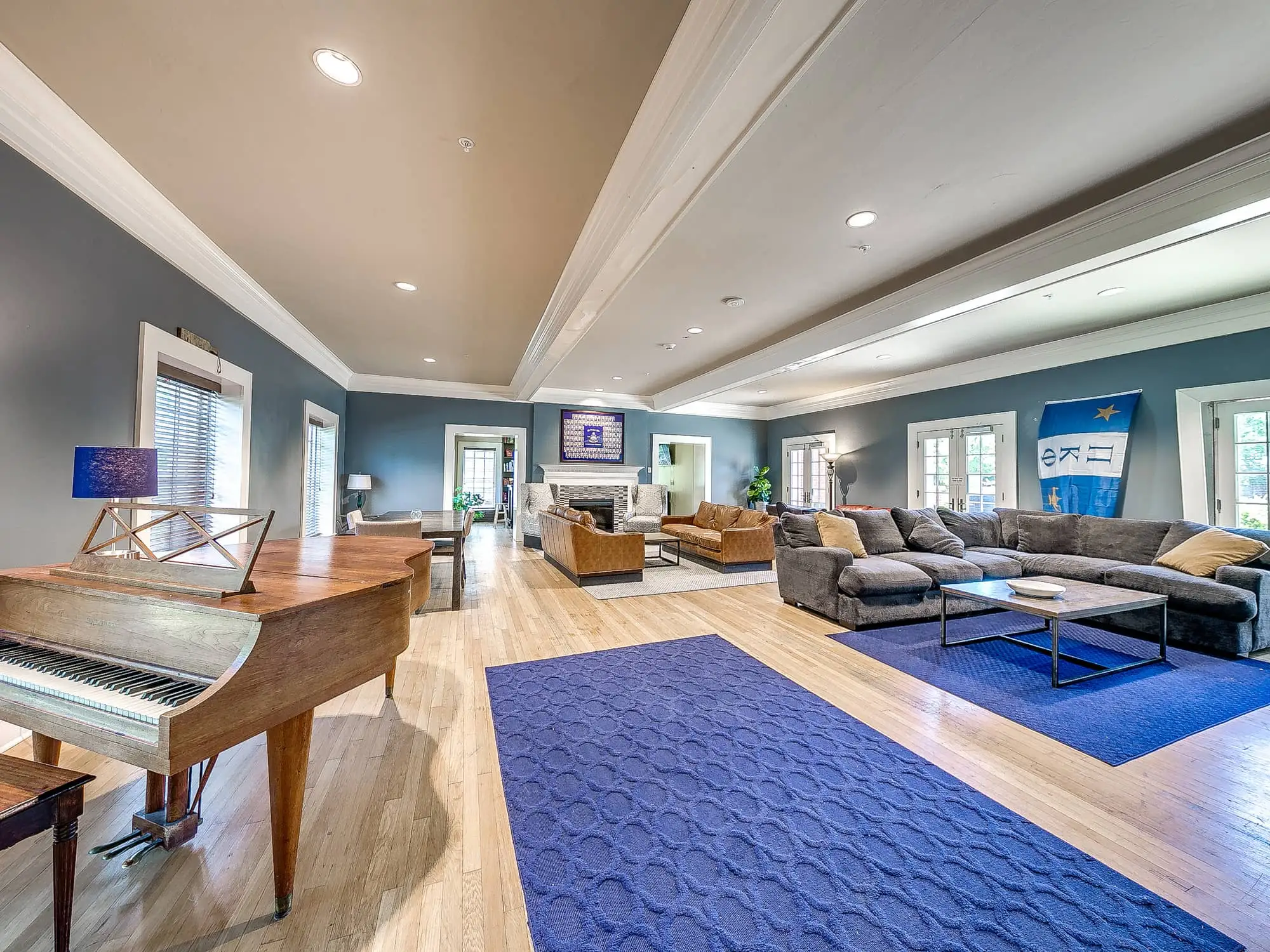 The main living room, with a grand piano, hardwood floors, sectional seating and a fireplace at the far end